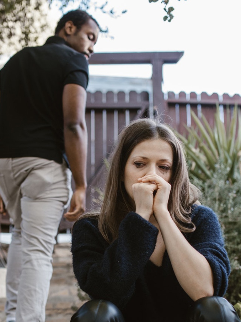 Gekwetste vrouw treurt terwijl partner met sexverslaving wegstapt.